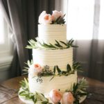 A three tiered Quinceanera cake on a wooden table adorned with olive leaves