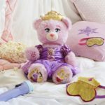 A plush teddy bear sitting on top of a bed next to pillows for a Quinceanera celebration