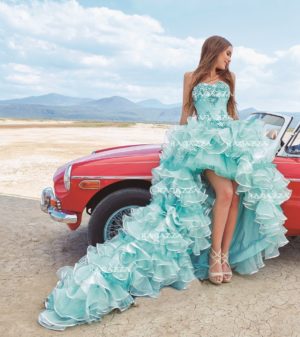 A woman in a blue Quinceañera gown sitting on a red car