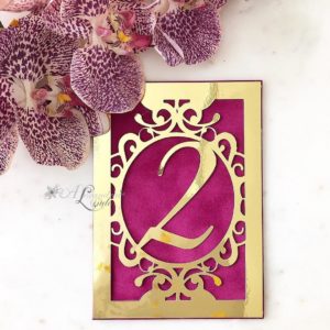 A lilac table with a pink and gold table number, surrounded by orchids in the background, perfect for a Quinceanera celebration.