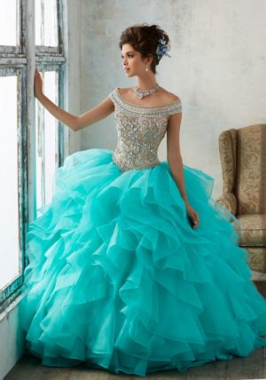 A woman in a blue Quinceañera dress standing in front of a window. The dress is from the Morilee collection, style 89138.