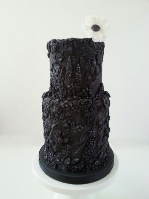 A Quinceanera cake displayed in the museum of fine arts. The cake is black with a white flower on top.