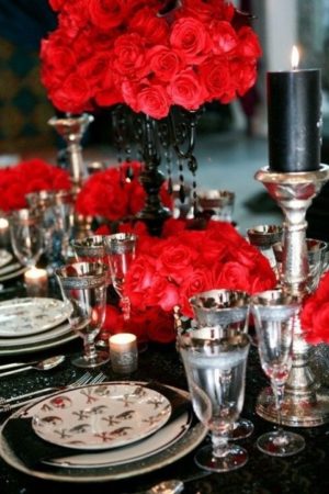 A Quinceanera centrepiece with a black table topped with silver plates and adorned with red flowers in a floral design.