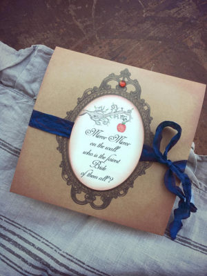 A Quinceanera invitation featuring a snow white theme. The invitation is a brown card with a blue ribbon and a picture of an apple.