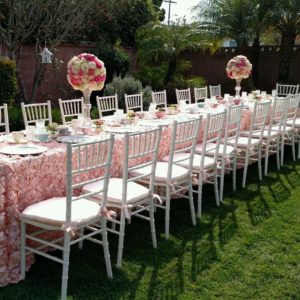 A long table with white chairs and pink tablecloths, perfect for a Quinceanera celebration.