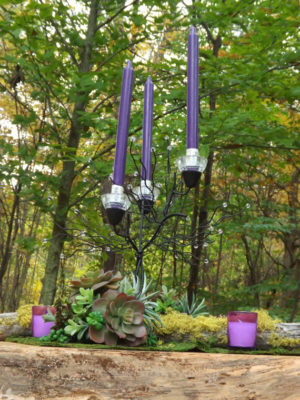 A purple candle holder with purple candles placed amidst a forest in a beautiful Quinceañera setup