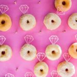 A bunch of Quinceanera-themed doughnuts arranged on a pink surface