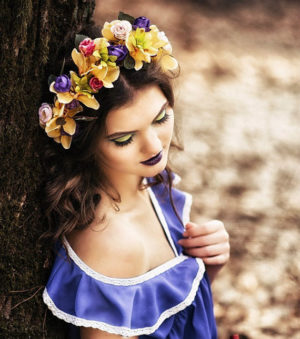 A Quinceanera woman with brown hair wearing a flower crown, leaning against a tree