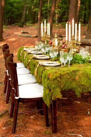 A quinceanera table set up with moss covered table, white chairs, and candles