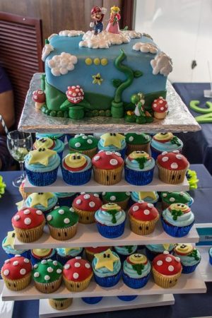 A Quinceanera-themed image featuring a Super Mario cake and cupcake tower. The cake is three-tiered and adorned with cupcakes.