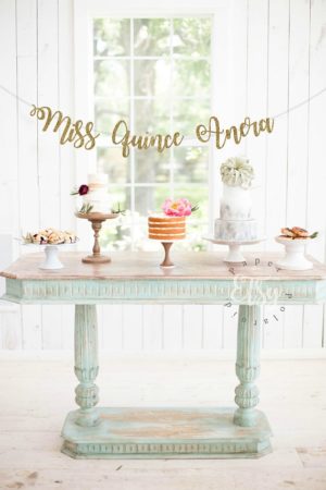 An interior design featuring a table with a cake and cupcakes on it for a Quinceanera celebration