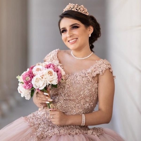 A woman in a pink quinceanera gown holding a bouquet and wearing earrings