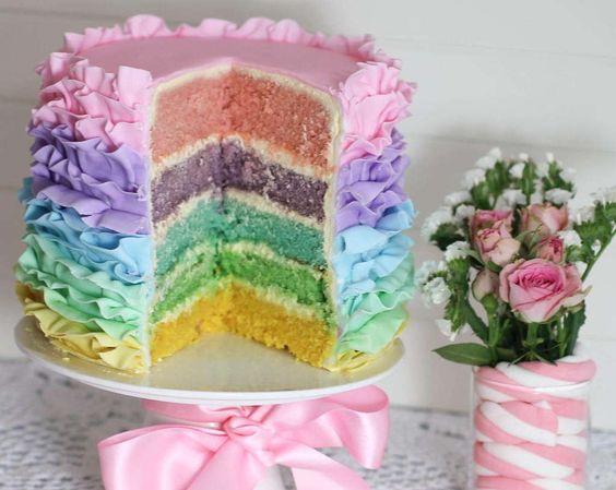 Quinceanera-themed pastel rainbow ruffle cake with a slice taken out of it