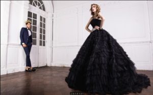 A couple dressed in elegant attire, with a woman wearing a black gown and a man in a tuxedo, posing together for a Quinceanera celebration