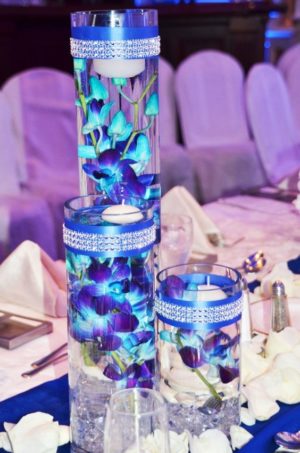 A Quinceanera table centrepiece featuring a vase filled with blue flowers, surrounded by royal blue and purple decorations.