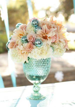 Quinceanera table decoration with pastel tones. A vase filled with flowers sits on top of a table.