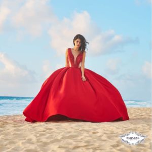A Quinceanera girl in a red dress sitting on a beach, wearing a fashionable gown