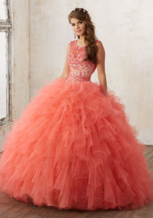 A woman in a coral and gold quinceanera dress standing in a room