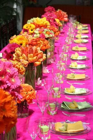 Quinceanera decorations, a long table is set with a pink table cloth and yellow and pink decorations