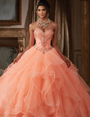 Quinceañera dresses in orange and a woman in a peach dress posing for a picture