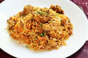 A Quinceanera themed photo of a white plate topped with rice and meat, known as biryani and mutton biryani, a traditional dish.