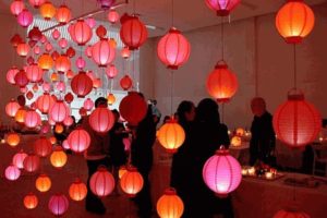 A quinceanera celebration with a group of people standing in a room filled with paper lanterns.