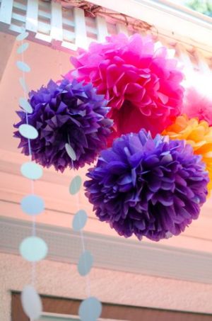 Floral design of cut flowers with a bunch of tissue pom poms hanging from a ceiling in a Quinceanera decoration