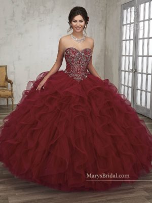 A woman wearing a burgundy strapless Quinceañera dress, posing for a picture in a red ball gown