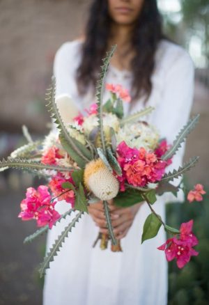 A woman in a white dress holding a bouquet of Quinceanera flowers, including cactus and other floral arrangements