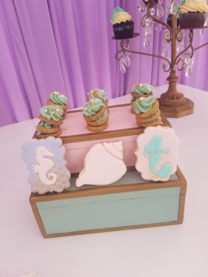 A Quinceanera cake with sugar decorations, surrounded by cupcakes and cookies on a table