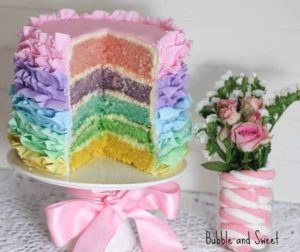 A Quinceanera themed buttercream pastel rainbow cake with icing, featuring a slice taken out of it