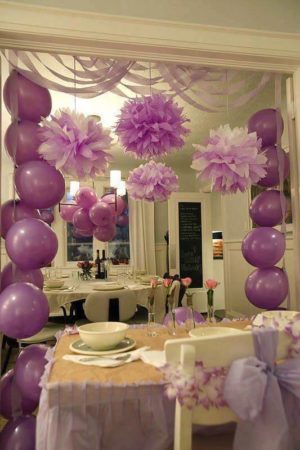 Quinceanera: A small house birthday party with a table adorned with a bunch of balloons hanging from the ceiling.