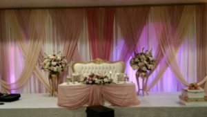 A Quinceanera function hall with a curtain backdrop and a table adorned with a bunch of flowers