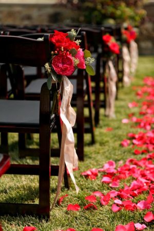 Quinceanera decoration with red roses - a row of wooden chairs with red flowers on them