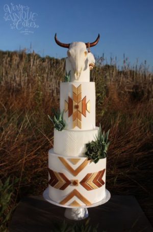 A Quinceanera cake featuring a three-tiered design with a cow skull on top