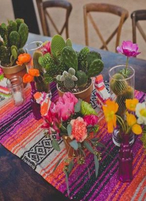Quinceanera image: a table topped with vases filled with flowers and decorated with Mexican table runners