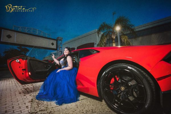 A Quinceanera woman in a blue dress sitting next to an electric blue sports car