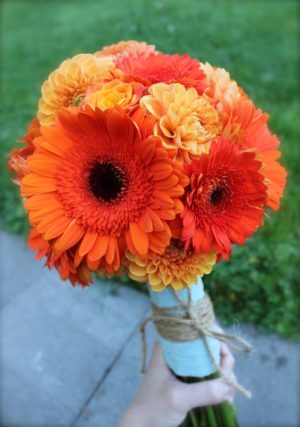A person holding a bouquet of orange and yellow flowers in a floral design