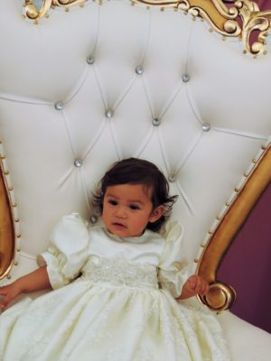 A little girl in a white Quinceanera dress sitting on a white chair during a Quinceanera party planning event.