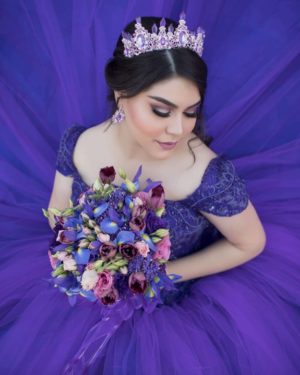 A woman in a purple Quinceanera dress holding a bouquet, with a beautiful bride hairstyle