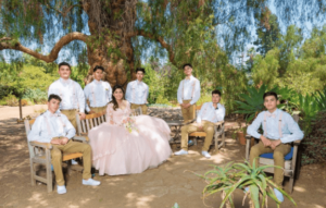 Group of people in formal attire posing for a picture with three Quinceañera dresses