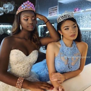 Two beautiful young women wearing tiaras posing for a picture with a stunning Quinceanera hairstyle