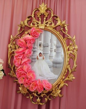 A picture frame display featuring a Quinceañera. In the mirror, there is a reflection of a woman in a Quinceañera dress.