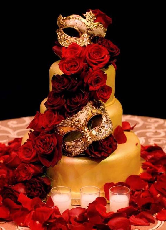 A Quinceanera cake decorated with red roses and a gold mask