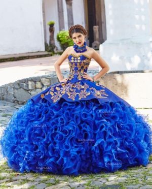 A woman in a royal blue Quinceanera dress with gold accents, posing for a picture in a charro-inspired Quinceañera dress.