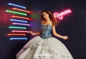 A woman in a white Quinceanera dress standing in front of a neon sign