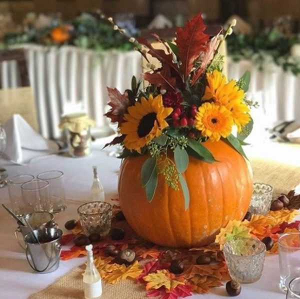 A Quinceanera themed centrepiece floral design featuring a table with a pumpkin decorated with flowers and leaves.