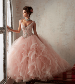 A woman in a pink Quinceañera dress standing by a window