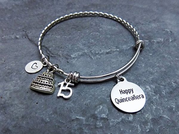 A silver bang bracelet with a cake charm and a happy quincclier charm, perfect for a Quinceanera celebration