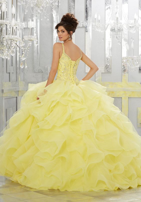 A woman in a yellow Quinceañera gown standing in front of a chandelier
